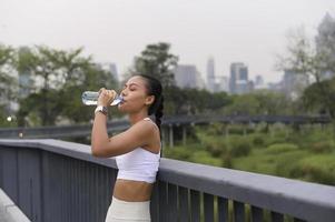 mulher jovem fitness em sportswear água potável no parque da cidade, saudável e estilos de vida. foto