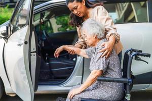 cuidador ajuda paciente idosa asiática com deficiência entrar em seu carro, conceito médico. foto