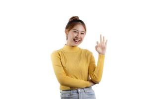 um retrato de uma linda mulher asiática em uma camisa amarela em pé posa para um sinal de mão okey. conceito de retrato usado para propaganda e sinalização, isolado sobre o fundo em branco, copie o espaço. foto