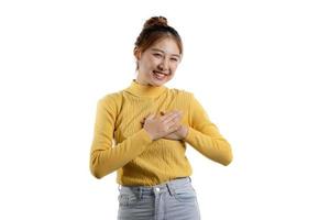 um retrato de uma linda mulher asiática em uma camisa amarela em pé com as duas mãos no coração. conceito de retrato usado para propaganda e sinalização, isolado sobre o fundo em branco, copie o espaço. foto