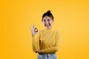 um retrato de uma linda mulher asiática em uma camisa amarela em pé posa para um sinal de mão okey. conceito de retrato usado para propaganda e sinalização, isolado sobre o fundo em branco, copie o espaço. foto