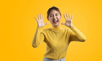 retrato de uma linda mulher asiática em uma camisa amarela em pé com as mãos para cima de alegria. conceito de retrato usado para propaganda e sinalização, isolado sobre o fundo em branco, copie o espaço. foto