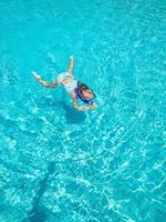 menina bonitinha na piscina clara nada debaixo d'água com equipamento de snorkel. férias de verão, viagens em família foto