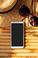 telefone inteligente de tela vazia com acessórios de viagem na mesa de madeira, conceito de férias de verão foto