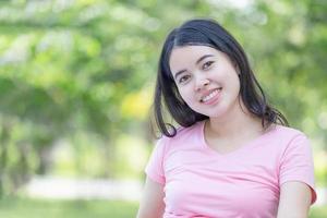 jovem alegre no parque, mulher sorridente relaxa e olhando para a câmera turva fundo verde foto