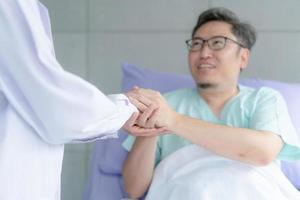 sorrindo agradecido homem doente segurando a apreciação da mão do médico para ajudar a apoiar os cuidados. obrigado médico ou enfermeiro. foto