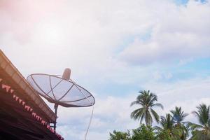 antena parabólica de tv na casa do telhado em rural com nuvens do céu e palmeira foto