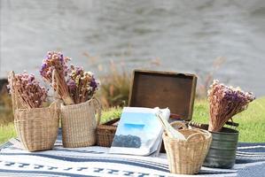 livro e cestas de flores na esteira azul com rio e floresta ao fundo. conceito de férias. foto