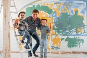 olhando para a câmera. homem com dois meninos em pé na sala doméstica. concepção de reparação e renovação foto