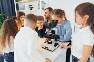 trabalhando com o microscópio. grupo de alunos de crianças em sala de aula na escola com professor foto