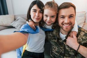 fazendo selfie. soldado de uniforme está em casa com sua esposa e filha foto