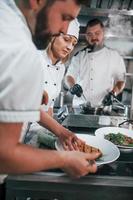 três pessoas vestindo juntos. chef profissional preparando comida na cozinha foto