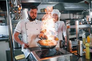 acender os alimentos na frigideira. chef profissional preparando comida na cozinha foto