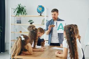 aprender uma nova carta. grupo de alunos de crianças em sala de aula na escola com professor foto