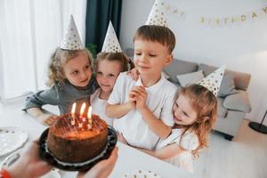 comemorando aniversário. mulher segurando o bolo. grupo de crianças está junto em casa durante o dia foto