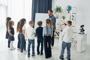 explicando a lição e usando o quadro. grupo de alunos de crianças em sala de aula na escola com professor foto