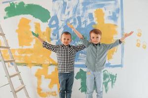 de pé juntos. dois meninos pintando paredes na sala doméstica foto