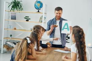 aprender uma nova carta. grupo de alunos de crianças em sala de aula na escola com professor foto