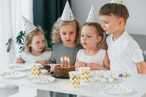 sentado à mesa com bolo. comemorando aniversário. grupo de crianças está junto em casa durante o dia foto