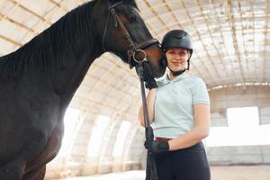 humor positivo. pronto para o treino. uma jovem com roupas de jóquei está se preparando para um passeio com um cavalo em um estábulo foto