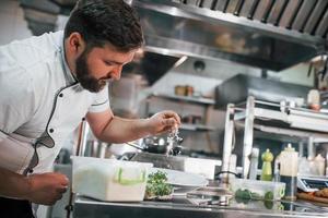 homem porando um pouco de sal. chef profissional preparando comida na cozinha foto