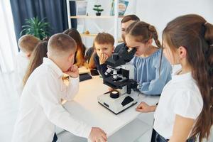 garota olhando no microscópio. grupo de alunos de crianças em sala de aula na escola com professor foto