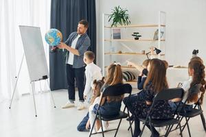 ensinando aula de geografia usando o globo terrestre. grupo de alunos de crianças em sala de aula na escola com professor foto