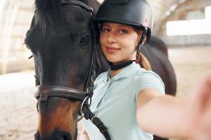 fazendo selfie. uma jovem com roupas de jóquei está se preparando para um passeio com um cavalo em um estábulo foto