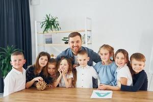 em pé e posando. sorrindo juntos. grupo de alunos de crianças em sala de aula na escola com professor foto