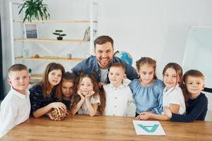 em pé e posando. sorrindo juntos. grupo de alunos de crianças em sala de aula na escola com professor foto