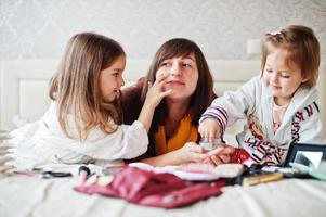 mãe e filhas fazendo maquiagem na cama no quarto. foto