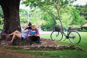 um homem lê um livro e uma mulher lê um livro também. Eles estão apaixonados e relaxam no parque público da Tailândia. Eles são o dia da lua de mel. foto