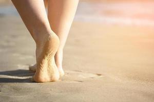 os pés descalços da menina na areia do mar close-up foto