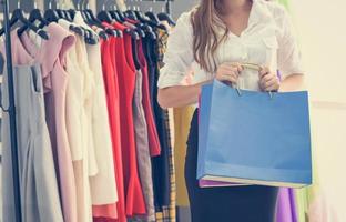 mulher fazendo compras e segurando sacola de compras em loja de roupas de moda feminina com vestidos coloridos femininos em cabides em uma loja de varejo de moda e compras