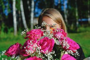 linda loira se escondendo atrás de rosas cor de rosa. foto