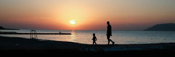 pai e filho caminhando juntos à beira-mar. foto