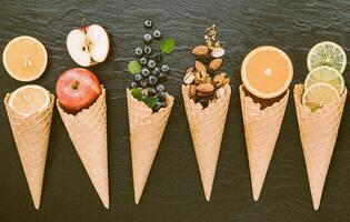 vários ingredientes para sabor de sorvete em cones montados em fundo escuro de pedra. foto