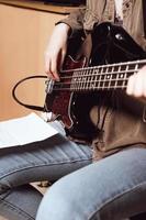 vista de corte de uma jovem tocando guitarra elétrica. baixista lendo notas de acordes e tocando em estúdio foto