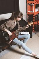 jovem tocando baixo e olhando para notas de acordes. Sala de ensaios. músico de rock feminino. tamanho vertical foto