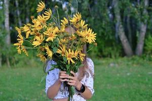 menina se escondendo atrás de um buquê de flores de topinambur. foto