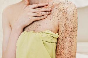 mulher aplicando esfoliante corporal. polimento de café orgânico natural nas mãos e no peito de uma mulher. vista de corte. conceito de spa em casa foto