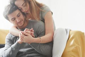 segurando pelas mãos. casal feliz relaxando no sofá amarelo na sala de sua nova casa foto