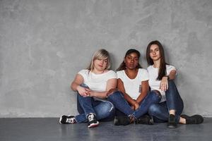 retrato de três pessoas. grupo de mulheres multiétnicas sentadas no estúdio contra um fundo cinza foto