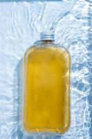 uma garrafa transparente de bebida de plástico é colocada na piscina de água. textura de superfície de água transparente de cor azul transparente com ondulações, salpicos e bolhas fundo da natureza ondas de água à luz do sol foto