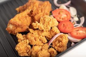 frango frito em uma panela preta com cebola e tomate fatiado foto