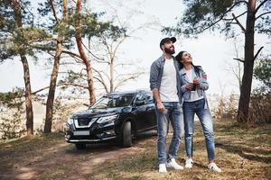 finalmente dia ensolarado. abraçando e curtindo a natureza. casal chegou à floresta em seu novo carro preto foto