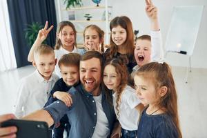 fazendo uma selfie por telefone. grupo de alunos de crianças em sala de aula na escola com professor foto