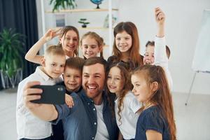 fazendo uma selfie por telefone. grupo de alunos de crianças em sala de aula na escola com professor foto