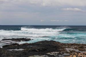 ondas oceânicas turbulentas com espuma branca batem nas pedras costeiras foto