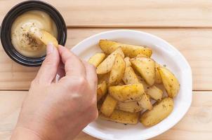 mão segurando batata frita com molho sobre mesa de madeira branca foto